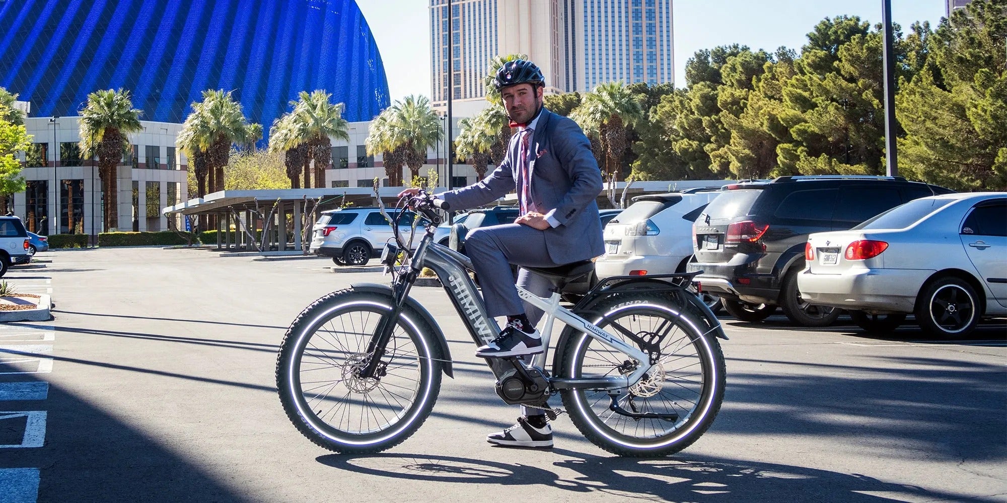 Man riding a bicycle on a city street with buildings and cars in the background