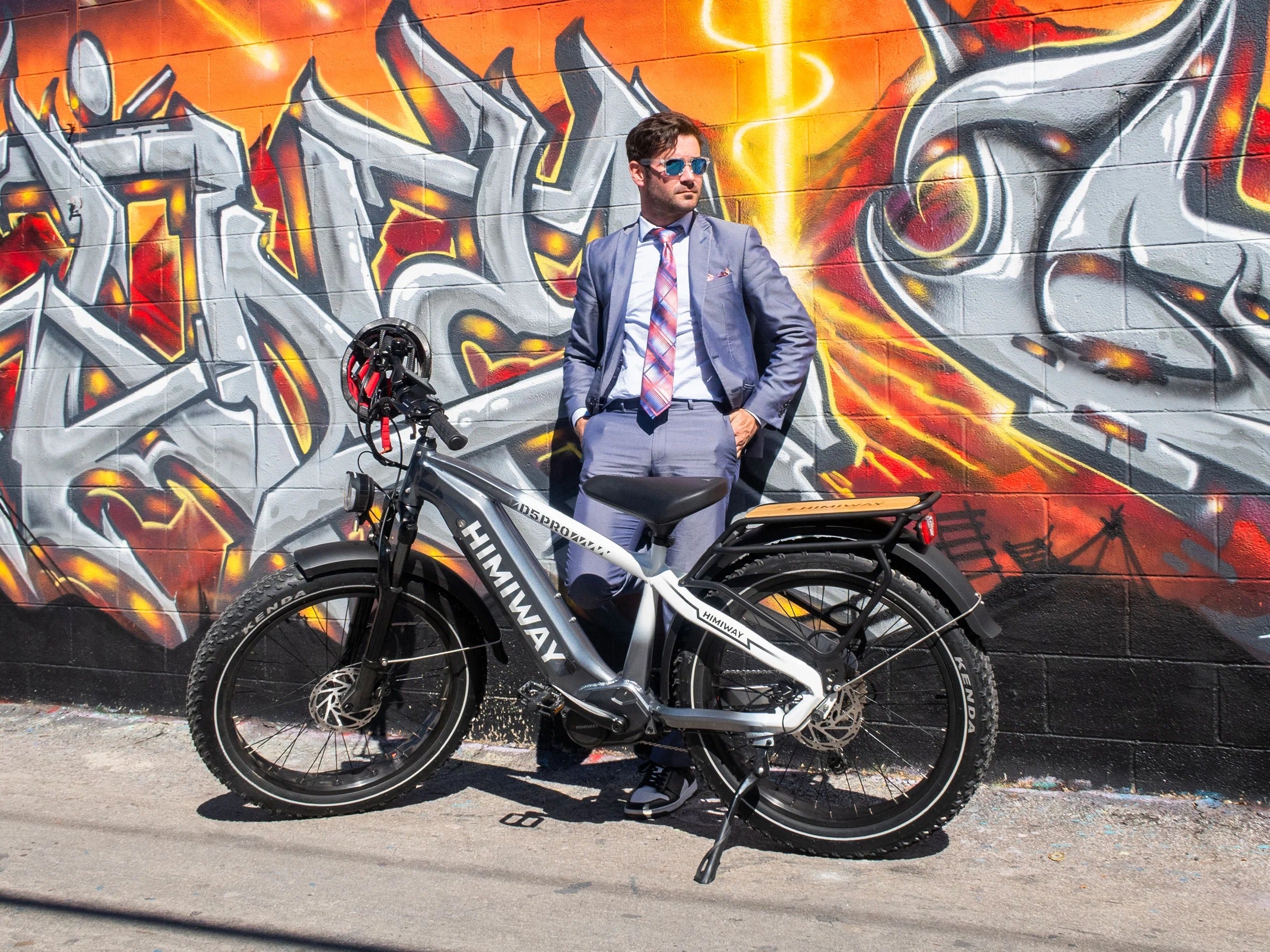 Man in a suit standing next to a electric bike with a colorful mural in the background