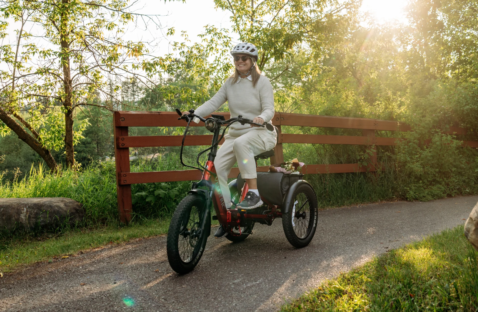 Person riding a tricycle on a path with trees and a wooden fence in the background