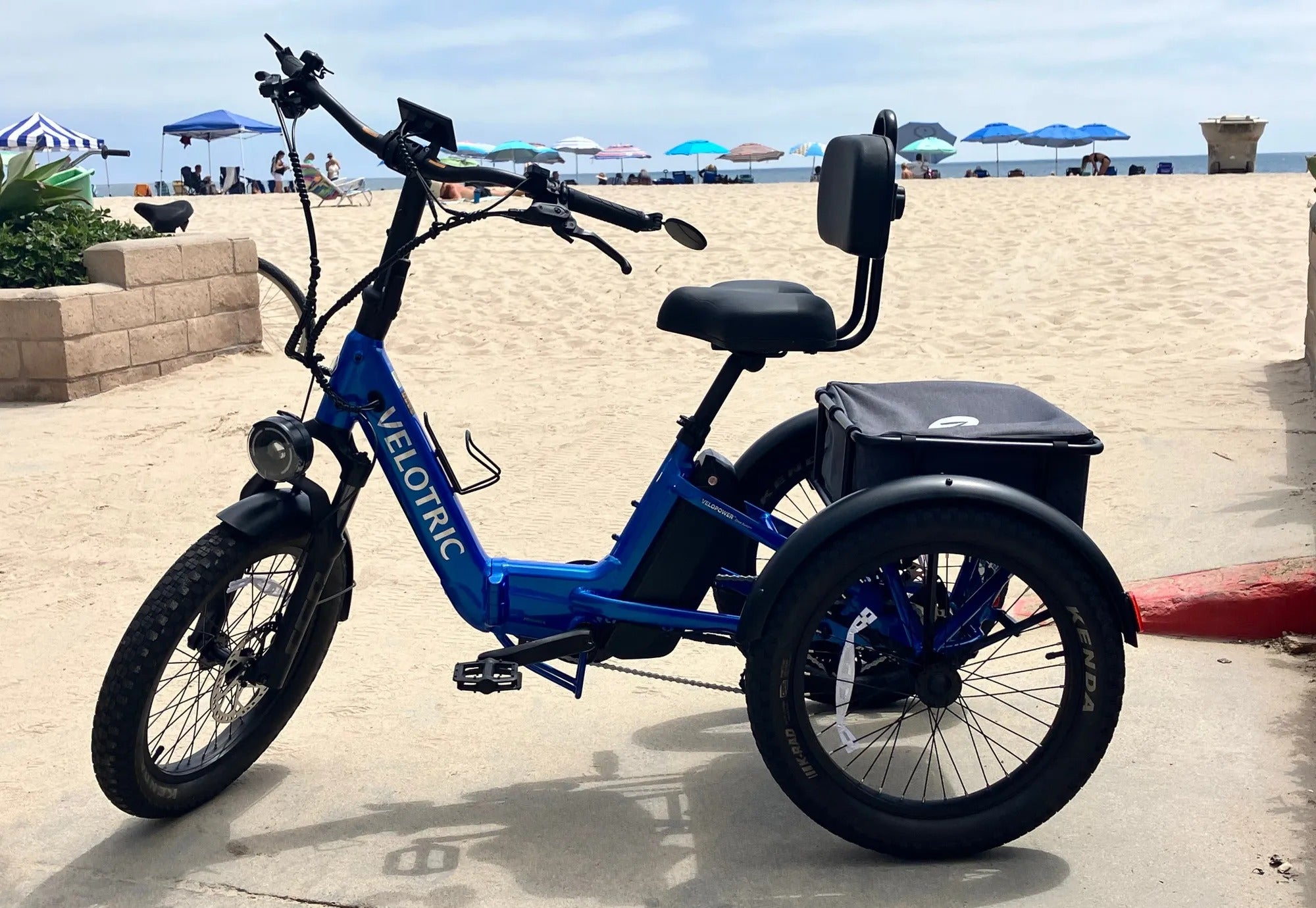 Blue electric tricycle on a beach with umbrellas and sand in the background
