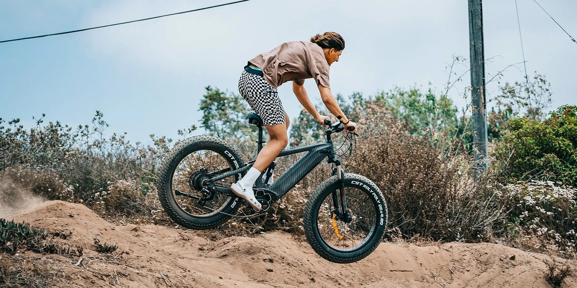 Person riding an electric bike on a dirt path with a clear sky and greenery in the background