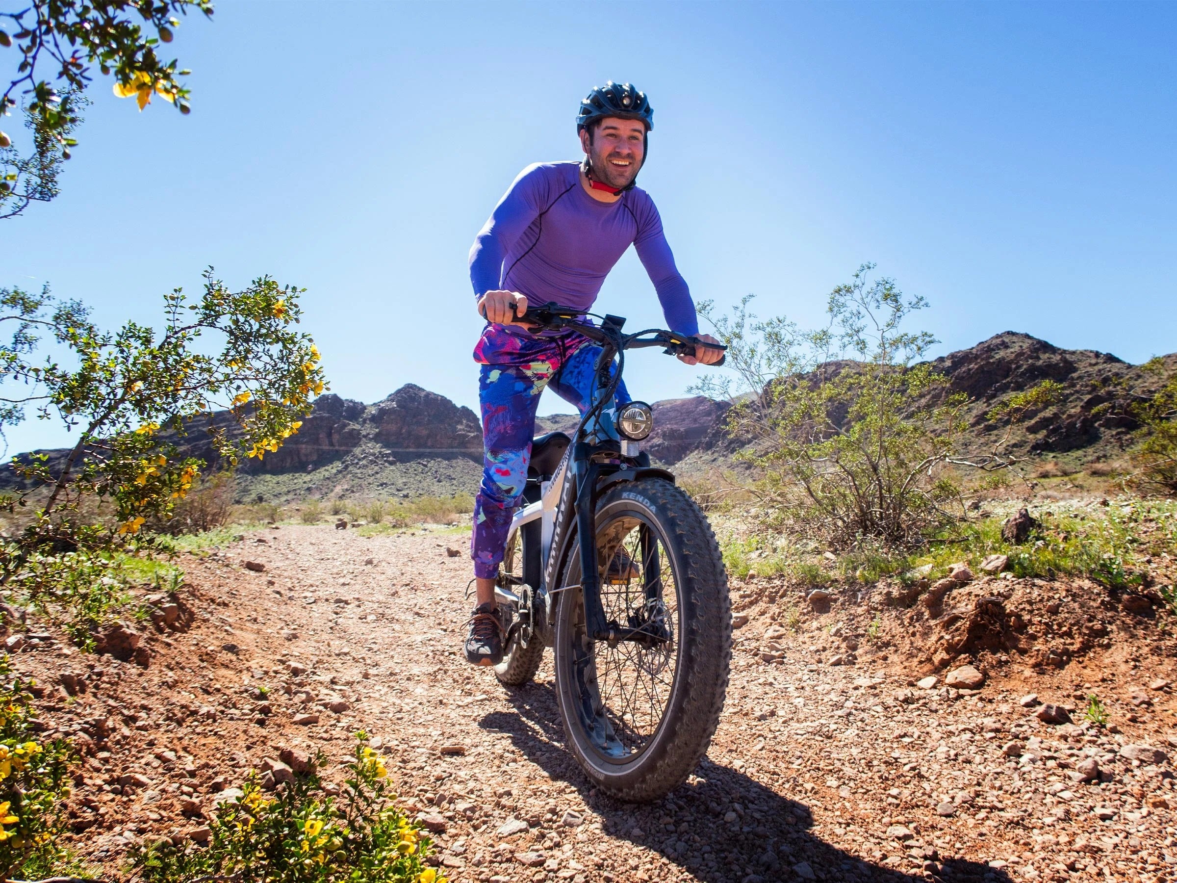 Man riding a mountain bike on a dirt trail with mountains in the background