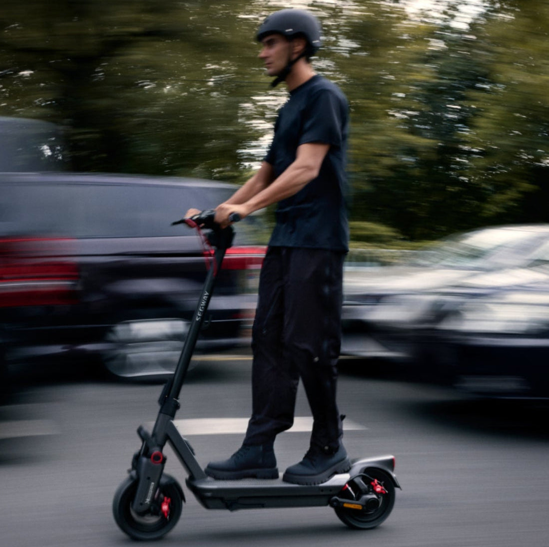 Person riding an electric scooter on a road with cars in the background