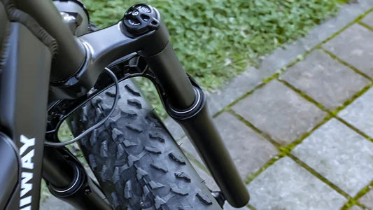 Close-up of a bicycle's suspension fork on a paved path with grass.